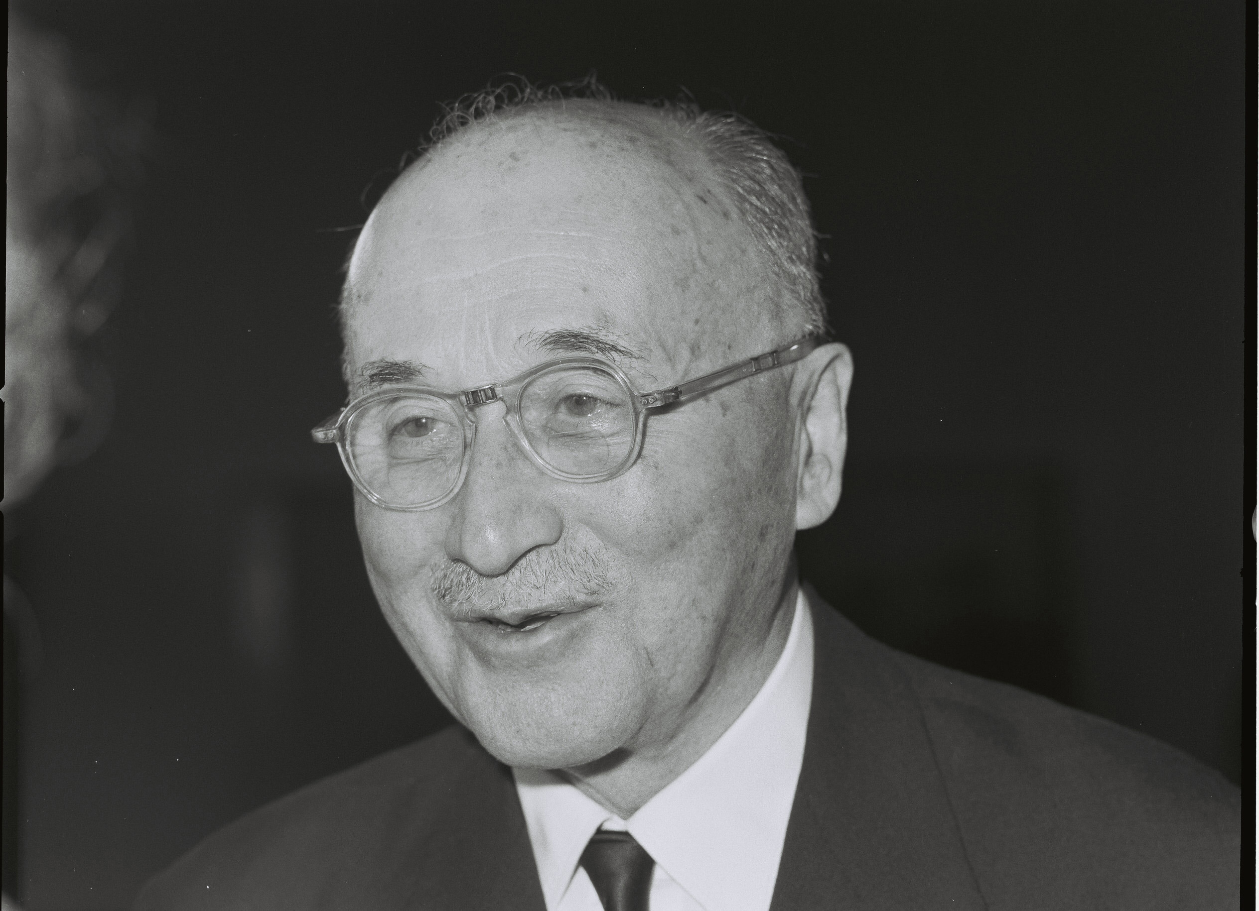 Black and white photo of Jean Monnet wearing a suit, smiling and wearing glasses