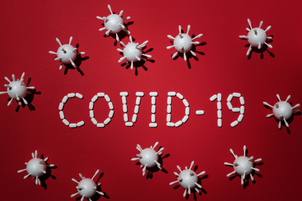Covid-19 skrivet i tabletter omgivet av modeller av coronavirus, på röd bakgrund