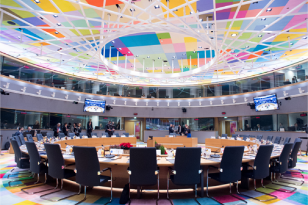 En sal inom EU med stort runt bord med stolar samt tolkbås och färgglatt tak